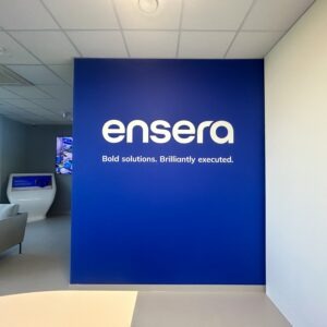 Niebieska ściana firmowa z białym drukowanym logo Ensera w strefie recepcyjnej nowoczesnego biura