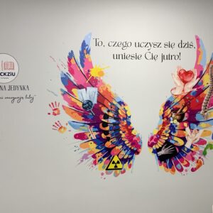 Kolorowe skrzydła wydrukowane bezpośrednio na ścianie dla WSCKZiU Nr 1 w Poznaniu, z symbolami medycznymi i hasłem „To, czego uczysz się dziś, uniesie Cię jutro!”.