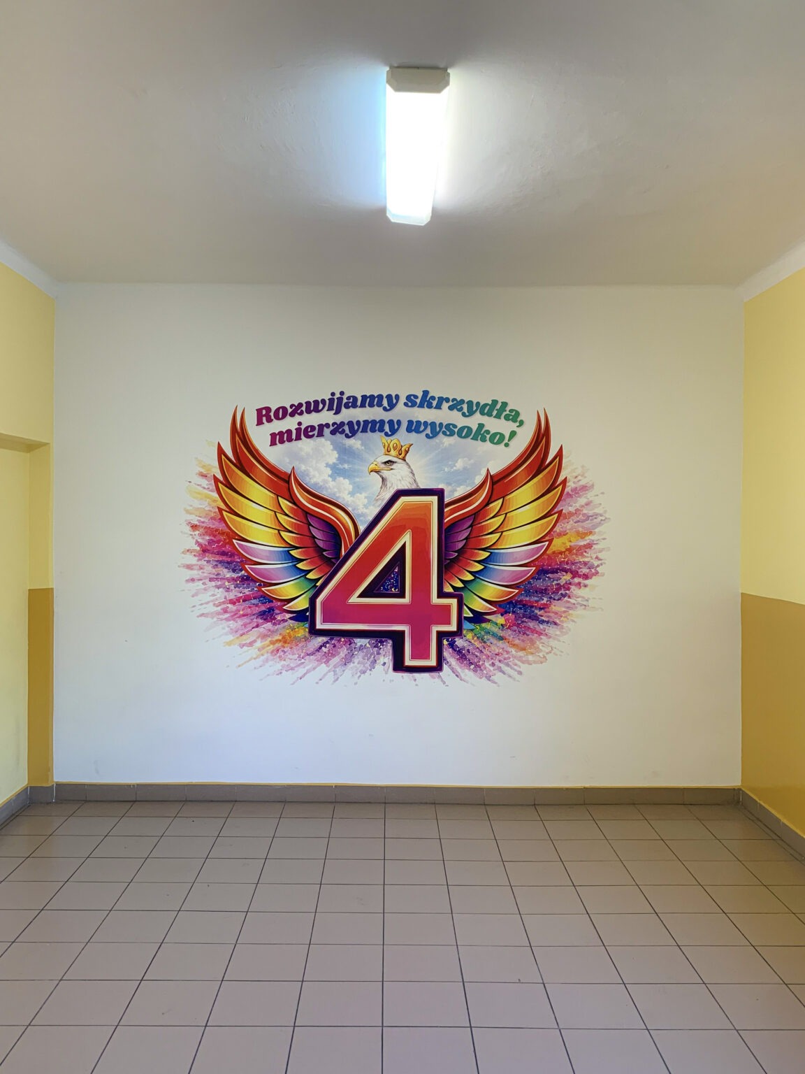 Kolorowy mural szkolny z liczbą 4, skrzydłami i napisem „Rozwijamy skrzydła, mierzymy wysoko!” wykonany technologią druku ściennego UV.