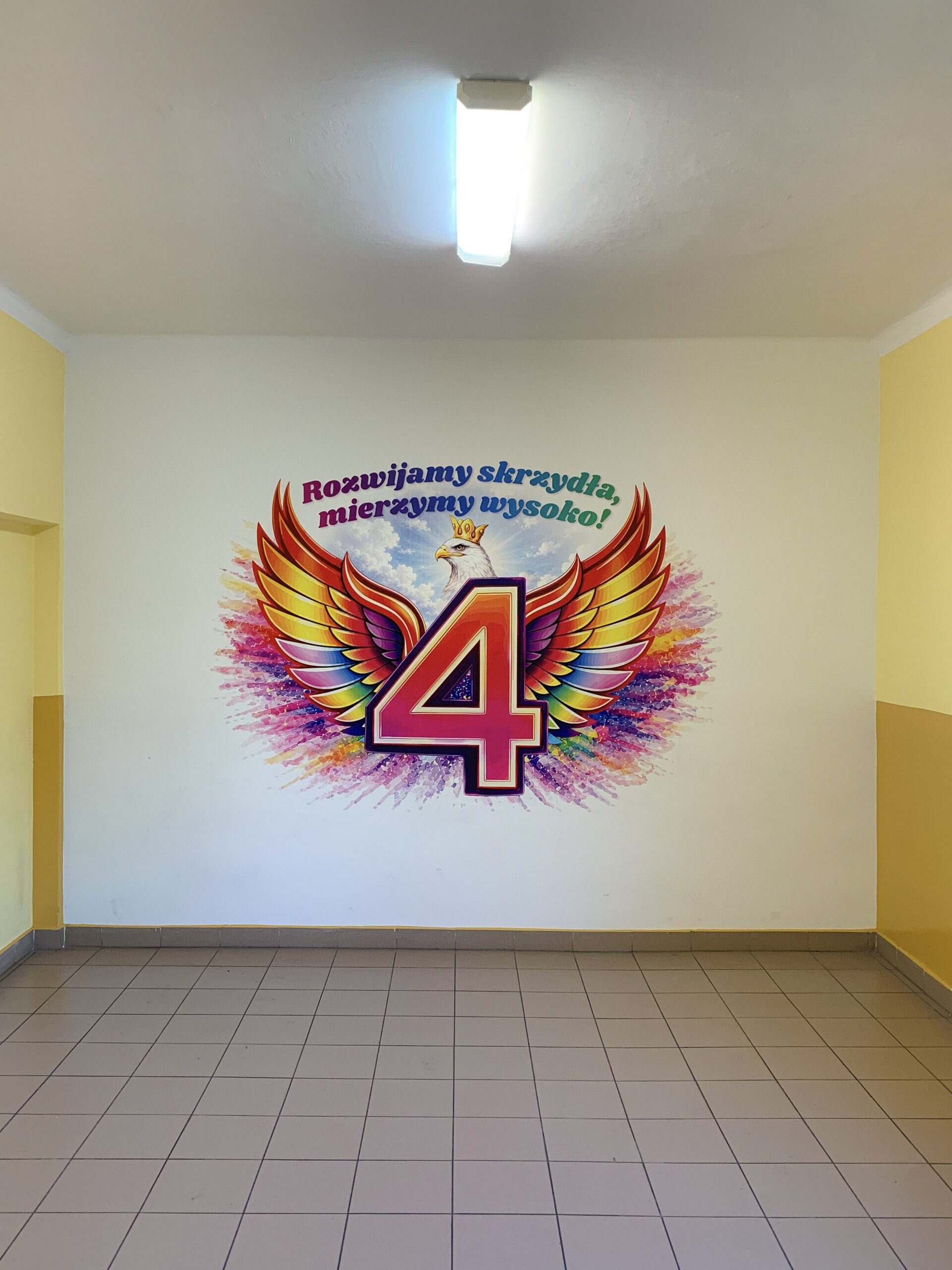 Kolorowy mural szkolny z liczbą 4, skrzydłami i napisem „Rozwijamy skrzydła, mierzymy wysoko!” wykonany technologią druku ściennego UV.